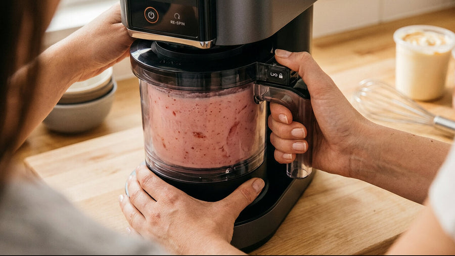 A person's hands visible twisting and locking the outer bowl of a Ninja Creami machine into place showing the correct assembly needed to fix a ninja creami too hard to spin error caused by an unlocked bowl.