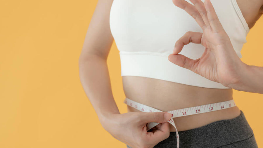 A woman's torso visible measuring her waist representing the importance of following proper GLP-1 protein tips to preserve muscle mass and lose fat rather than lean body mass on the medication.