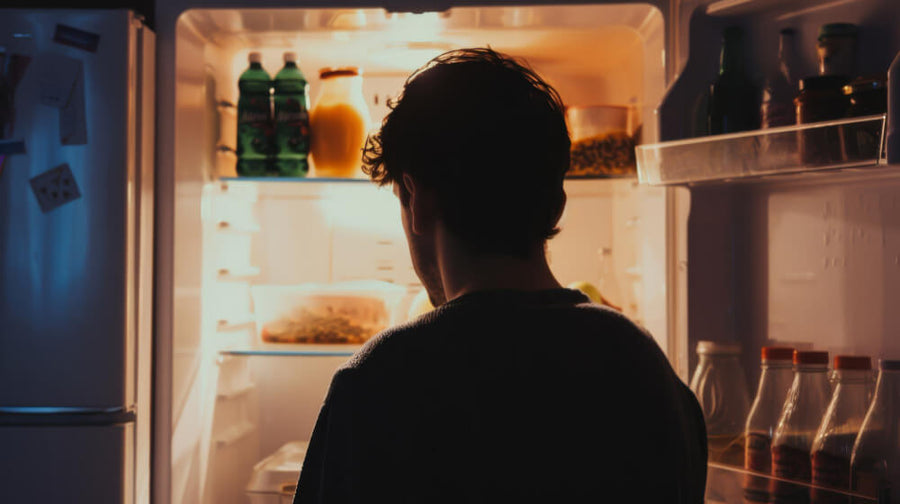 A person standing in front of an open refrigerator reaching for a Ninja Creami pint container showing one of the key ninja creami tips and tricks around freeze time.
