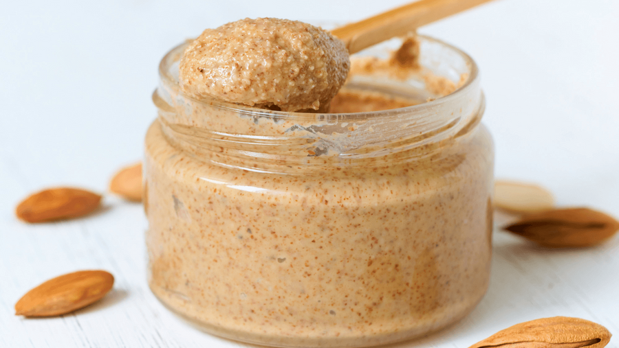 A spoonful of creamy nut butter beside a bowl of ice cream representing one of the richest healthy mix ins for a high protein frozen dessert.