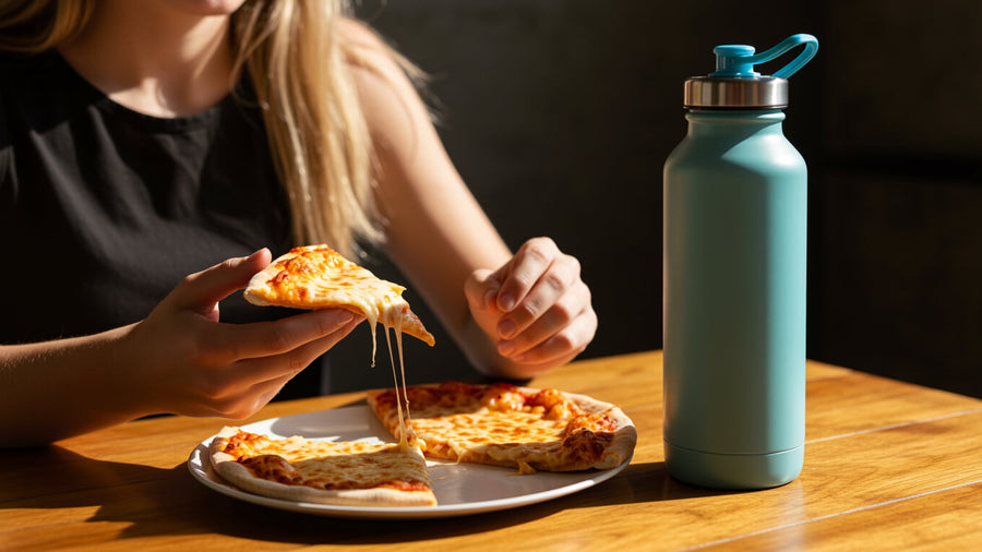 A person's hands visible eating a slice of pizza beside a gym water bottle showing why does cardio cancel out what you eat for weight loss is the wrong question to be asking.
