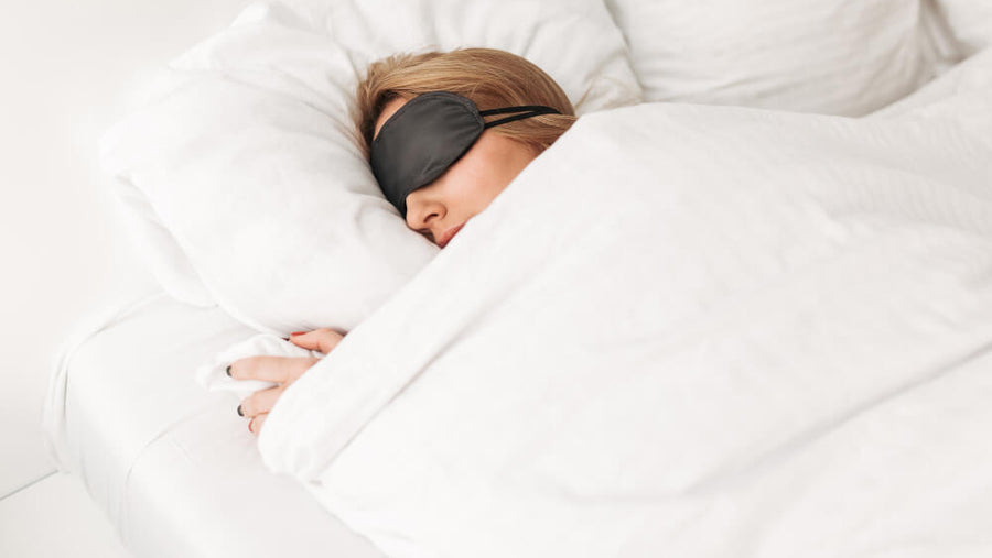 Person sleeping peacefully in bed wearing a sleep mask, representing deep overnight muscle recovery during sleep.