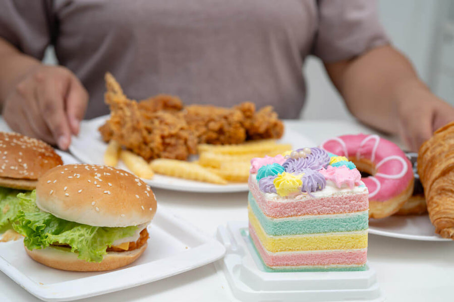 Plate of fried chicken, fries, burger, and colorful cake representing high-sugar and high-fat foods that disrupt sleep before bed