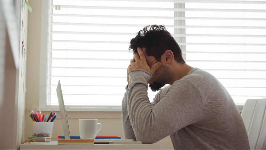 A stressed man's torso visible with his head in his hands representing how cortisol from daily stress amplifies why sugar cravings after eating hit hardest at the end of the day.