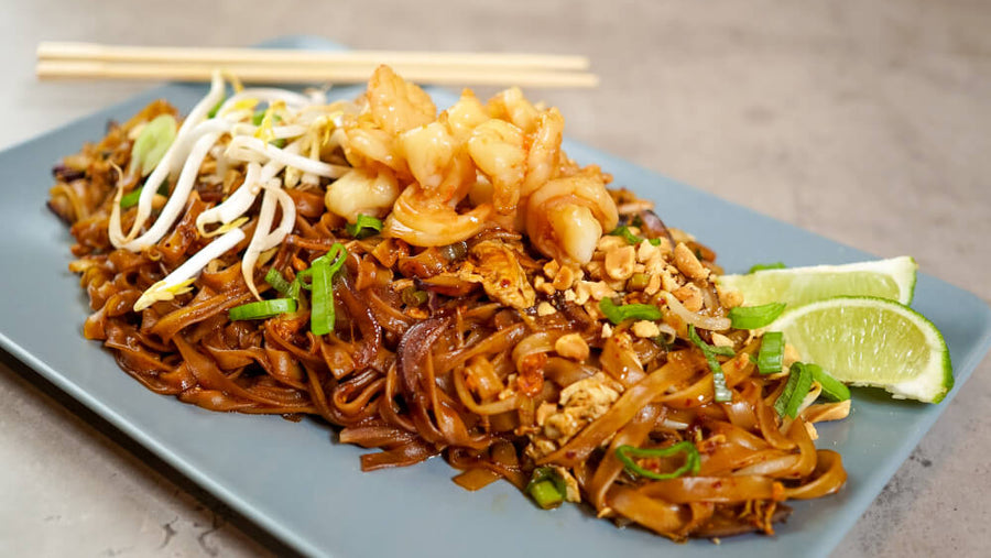 Close-up of pad thai noodles with shrimp, bean sprouts, and chopsticks on a plate.