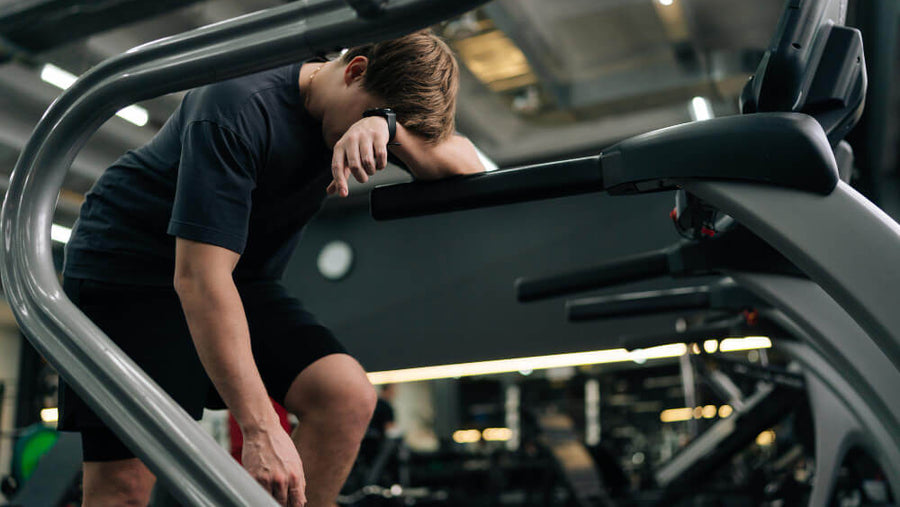 Person slumped over on gym equipment looking exhausted, representing how sleep debt reduces workout performance and training quality.