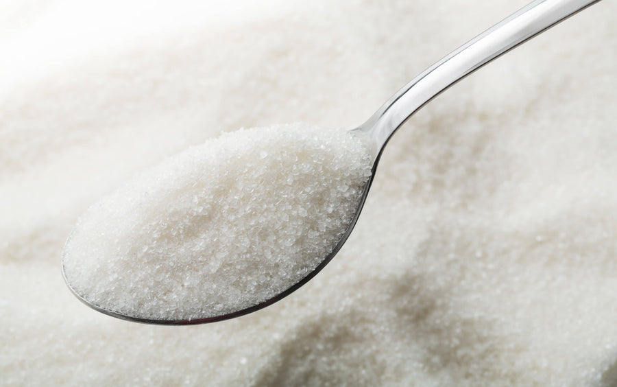 A metal spoon heaped with fine white sugar crystals representing allulose, a rare natural sugar used in low-glycemic ice cream.