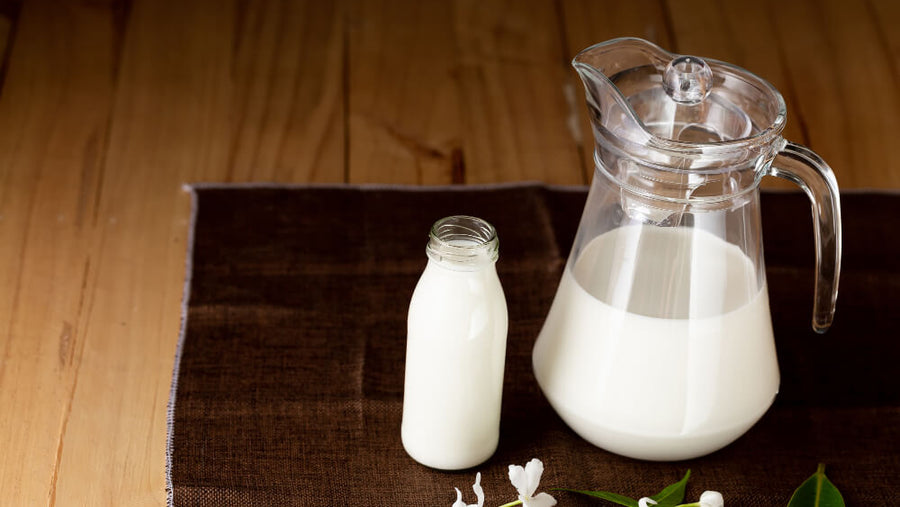 Glass pitcher and glass of whole milk on a dark wooden surface.